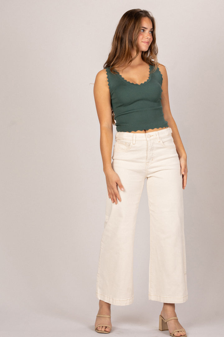 Woman wearing a green sleeveless top and white pants on a plain background