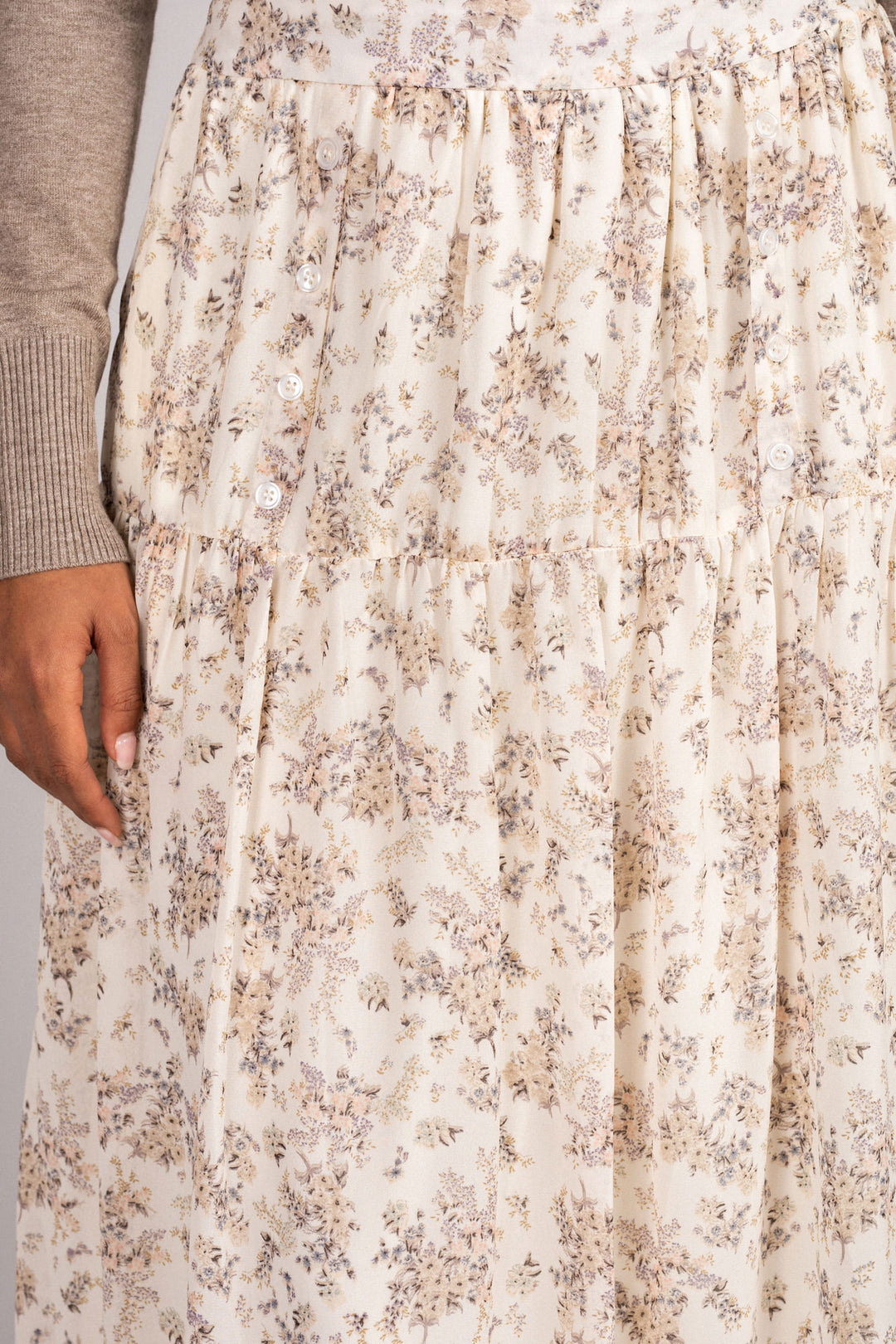 Ivory midi skirt with a subtle floral print pattern, featuring a tiered, button-down design and a relaxed, flowing silhouette.