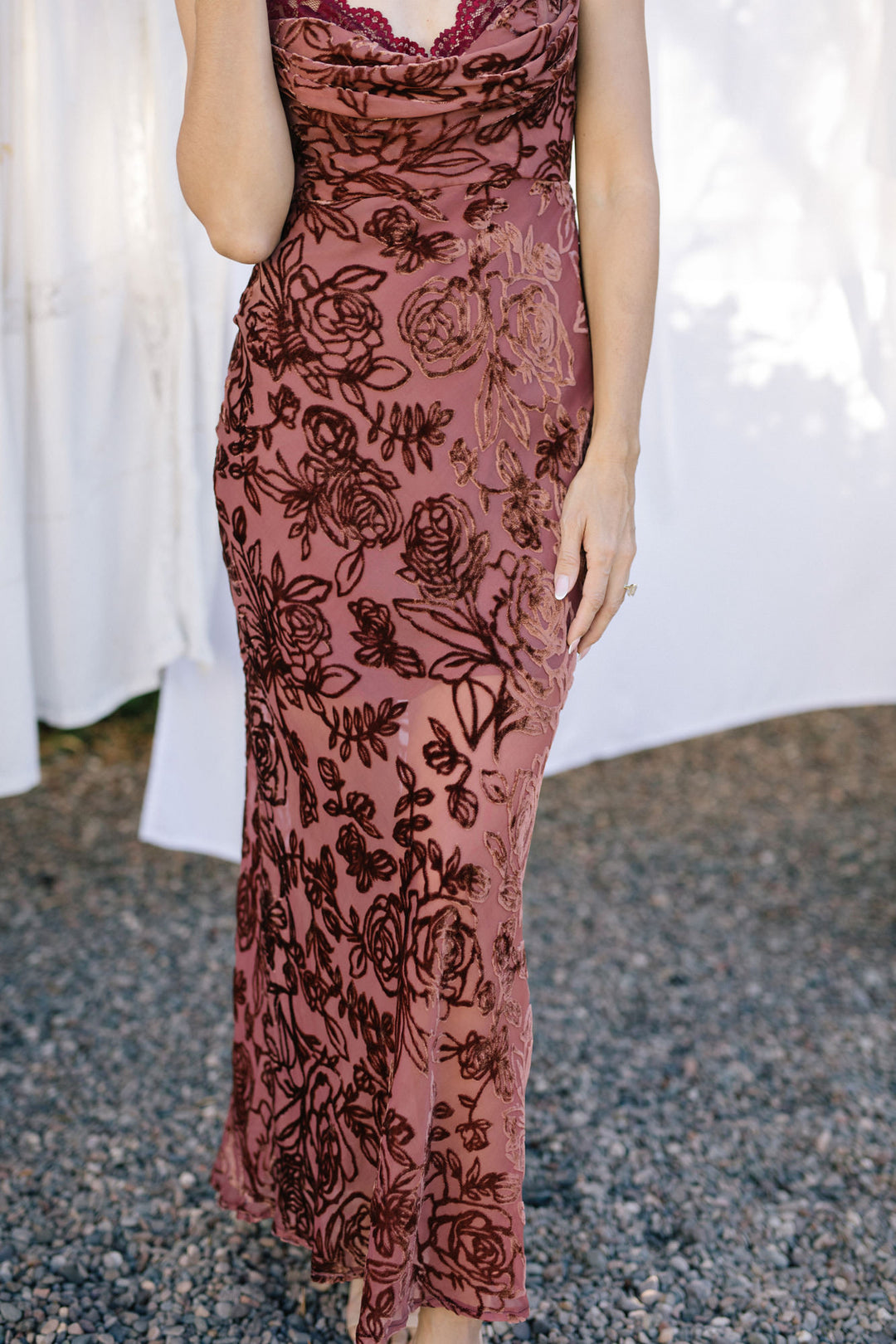 A close-up image of a sleeveless, burgundy-colored dress featuring an all-over floral print pattern and a cowl neckline design.