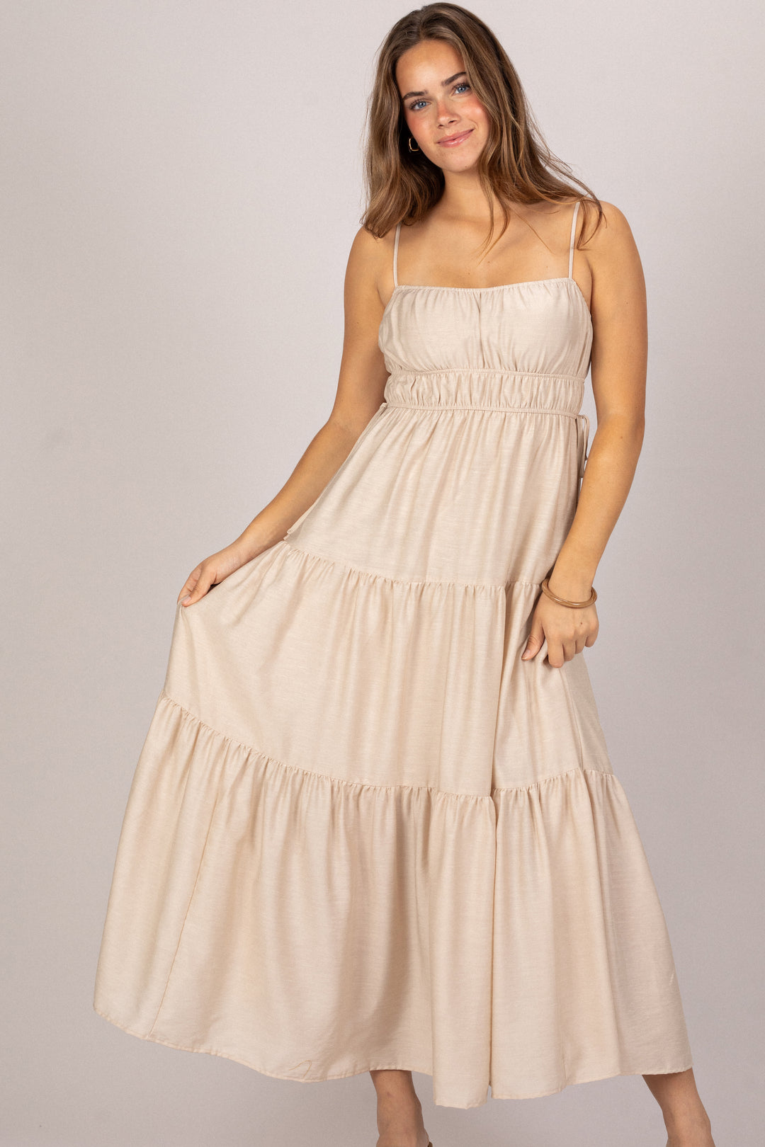 Woman wearing a beige tiered dress against a plain background