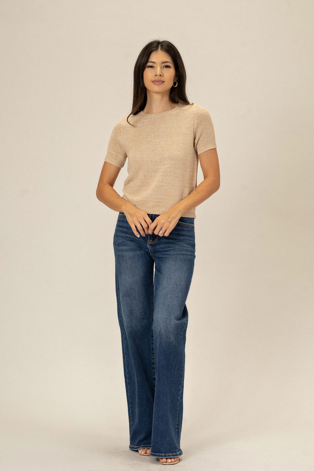 A petite woman in a beige knit top and blue jeans stands against a light background, presenting the Agnes Crew Neck Knit Tee.