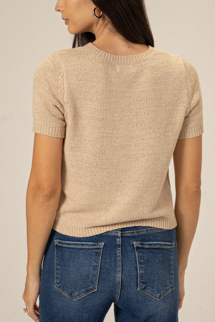Beige knit top with short sleeves and a crew neck, worn with blue denim jeans.