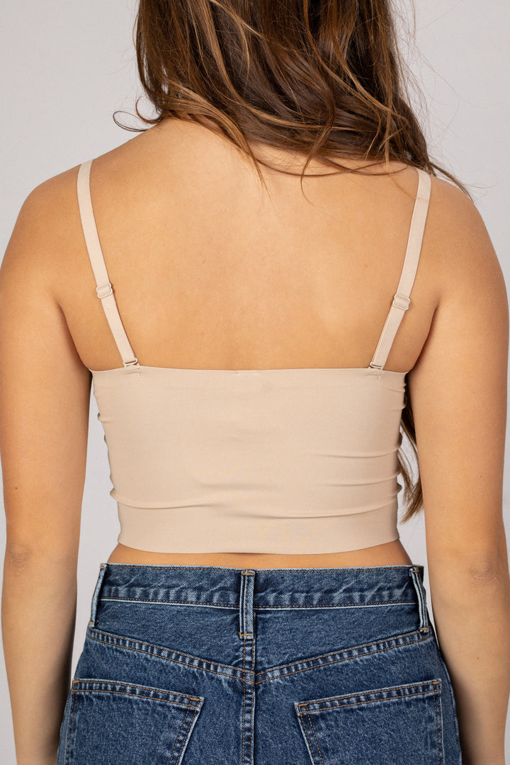 A beige seamless tank top with thin adjustable straps, showcasing a bare back and a fitted, cropped silhouette.