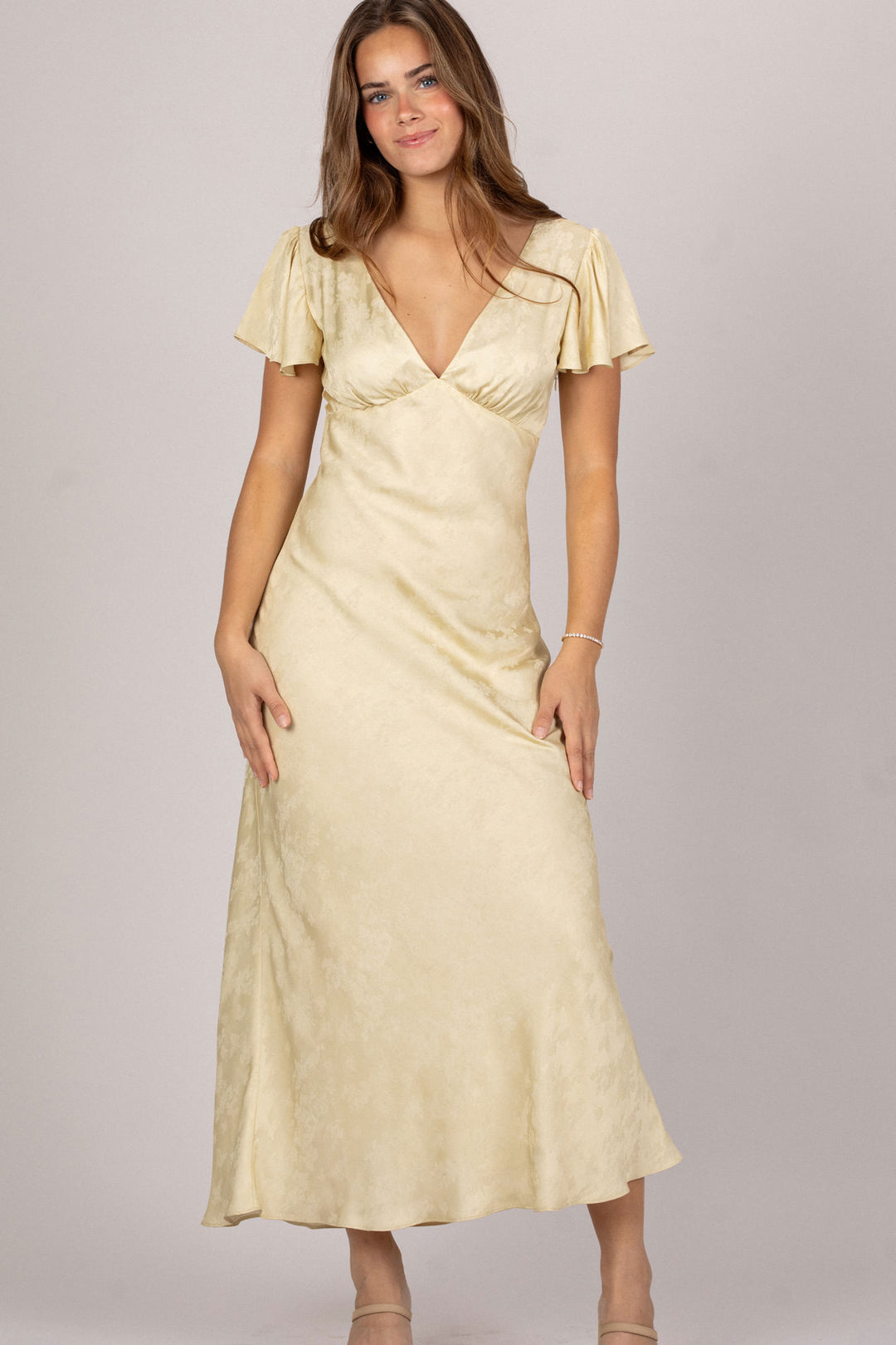 A sleeveless, floor-length dress in a pale yellow satin material with a deep neckline and short, fluttering sleeves.