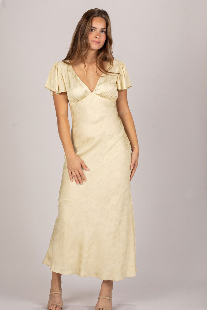 A woman wearing a long, soft yellow dress with short flutter sleeves and a v-neck bodice.