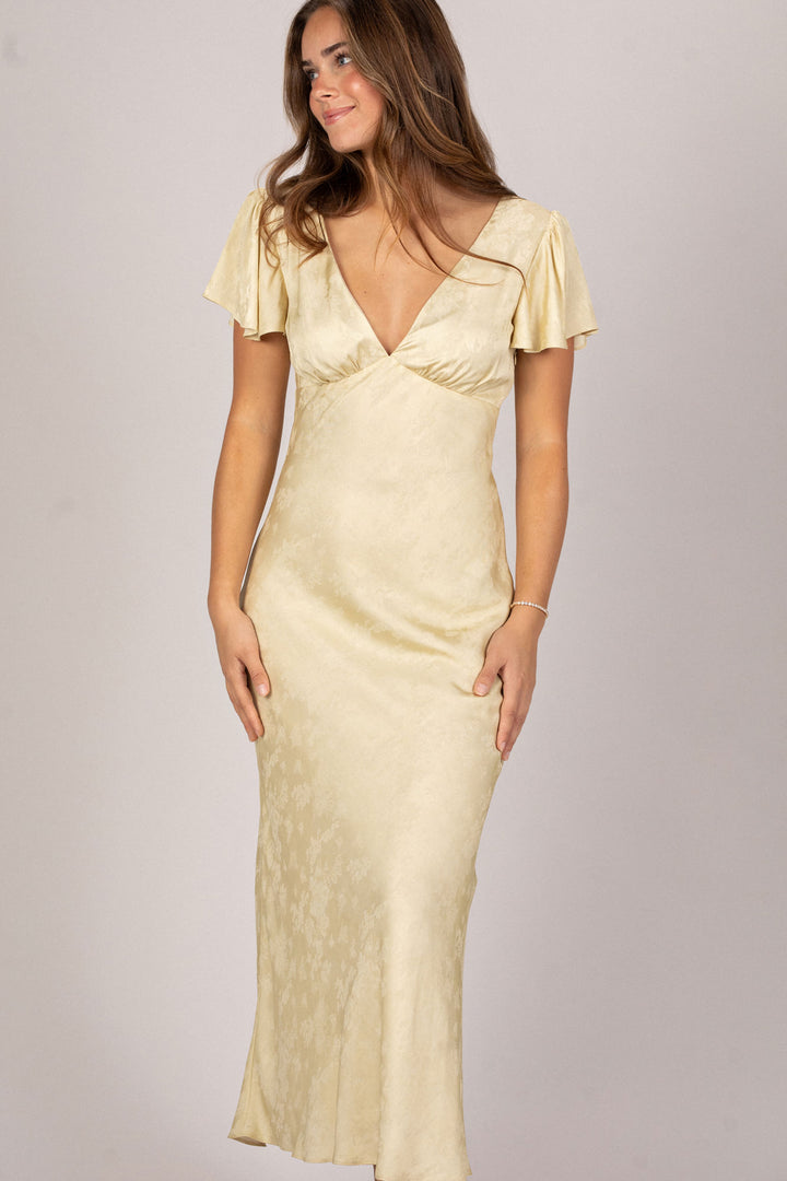 A long, flowing dress in a soft, pale yellow shade, featuring flutter sleeves and a plunging neckline, with a fitted waist and a flowing skirt.