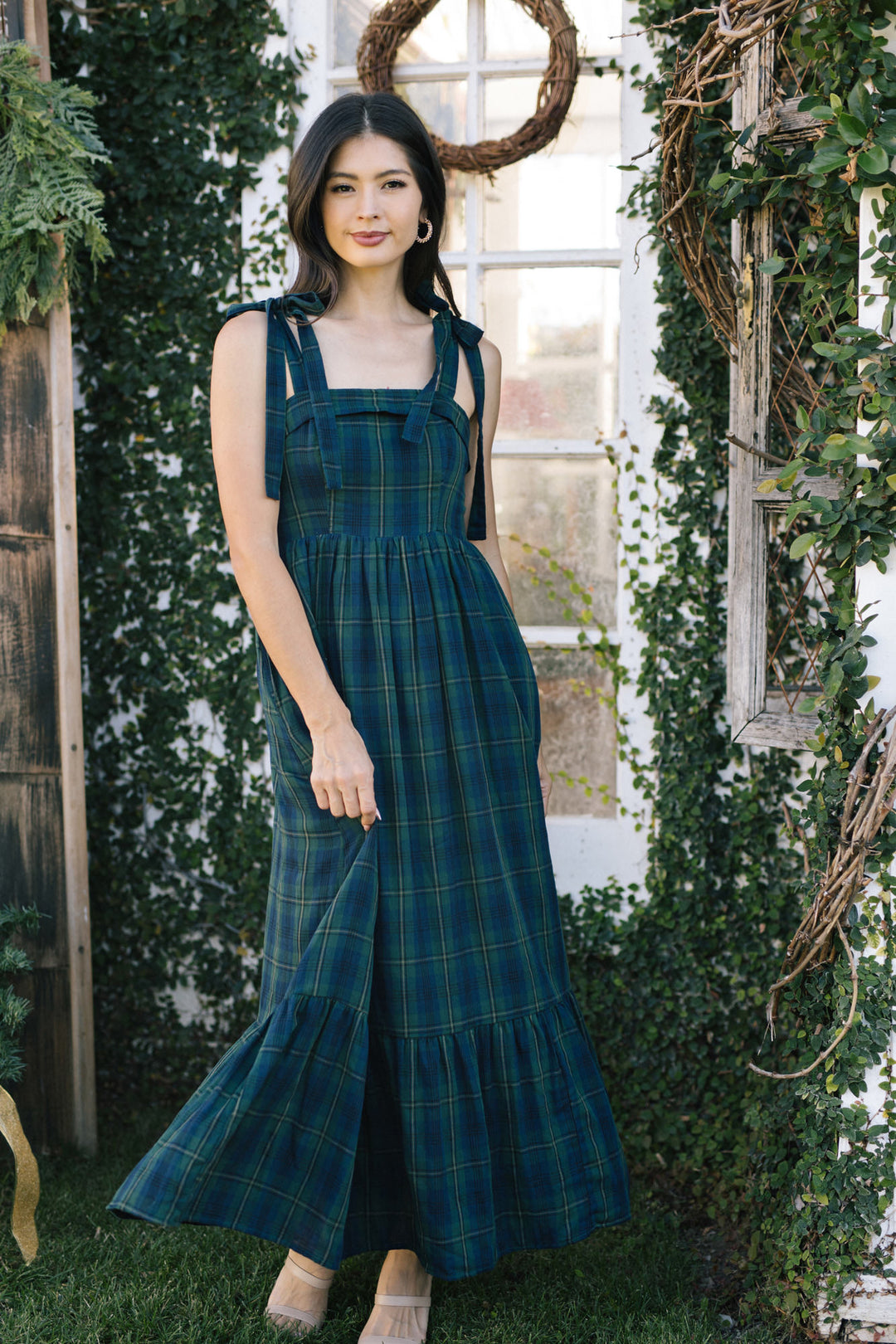 Green plaid maxi dress with ruffled sleeves and waist tie, worn by a young woman with long dark hair standing in a garden setting.
