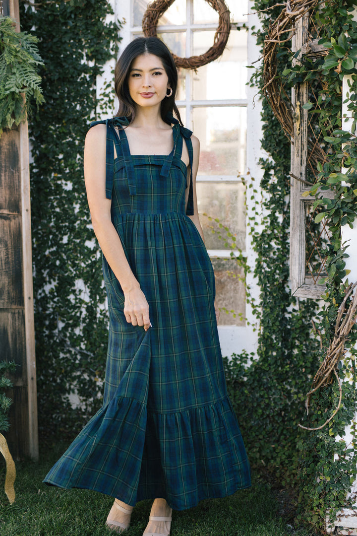 Green plaid maxi dress with ruffled sleeves and waist tie, worn by a young woman with long dark hair standing in a garden setting.