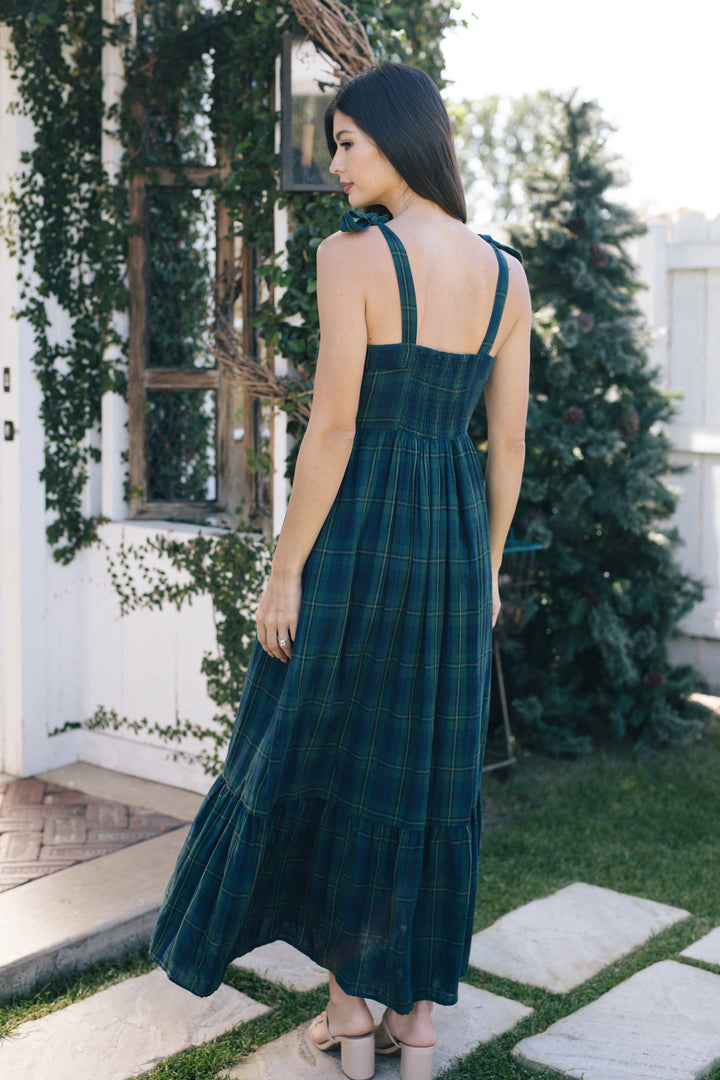 A full-length, sleeveless dress in a vibrant blue and green plaid pattern, featuring a fitted bodice and a flowing, tiered skirt.