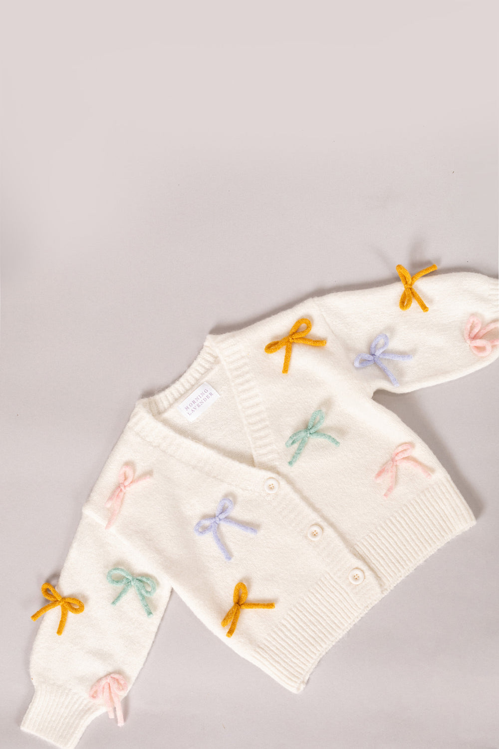 White knit cardigan with colorful bow and butterfly appliqués, suitable for toddler girls.
