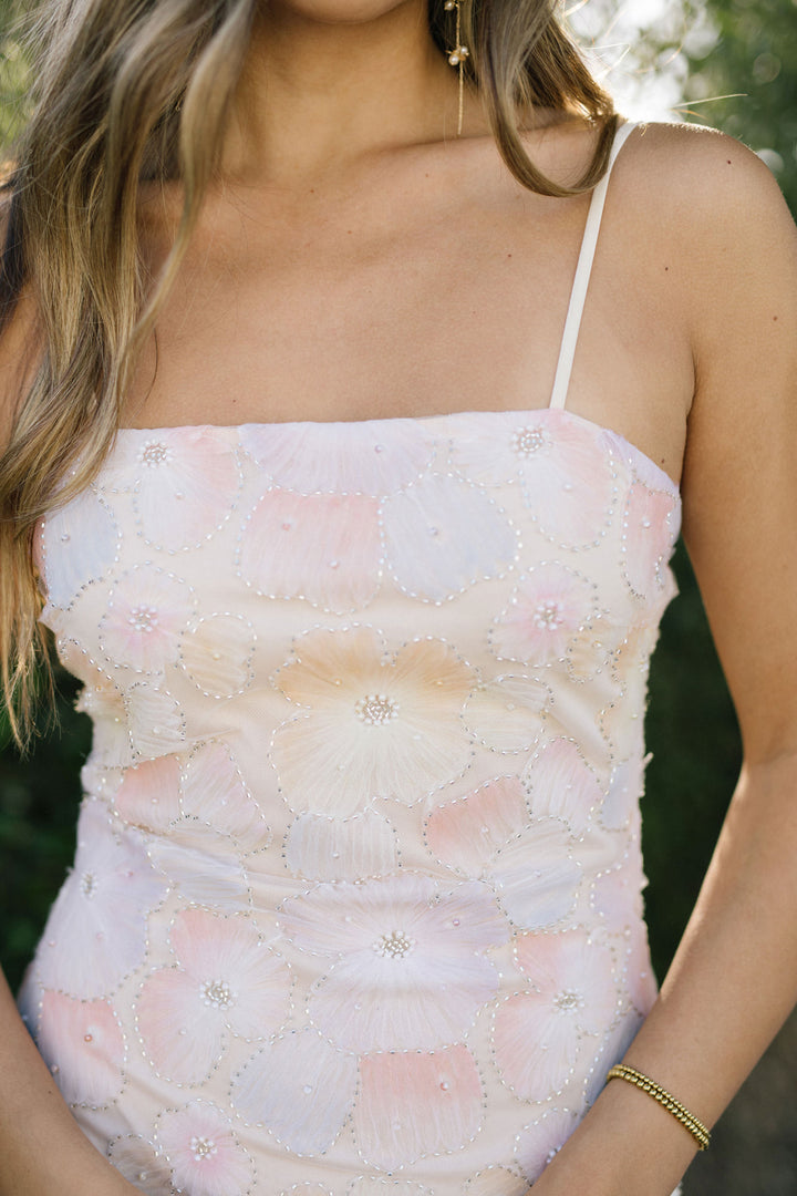 A white mini dress with intricate floral embroidery and shimmering sequin details, creating a romantic, feminine look.