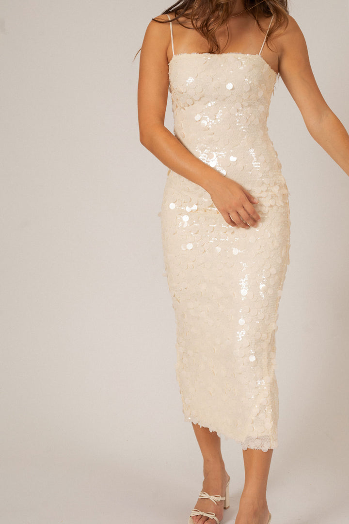 A sleeveless, midi-length sequin dress in a shimmering ivory color, featuring a fitted silhouette and spaghetti straps.