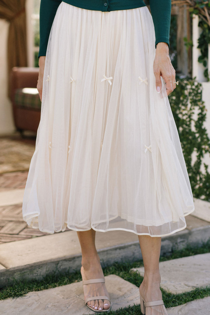 A flowing, white tulle midi skirt with small bows decorating the waistline, creating a delicate, feminine aesthetic.