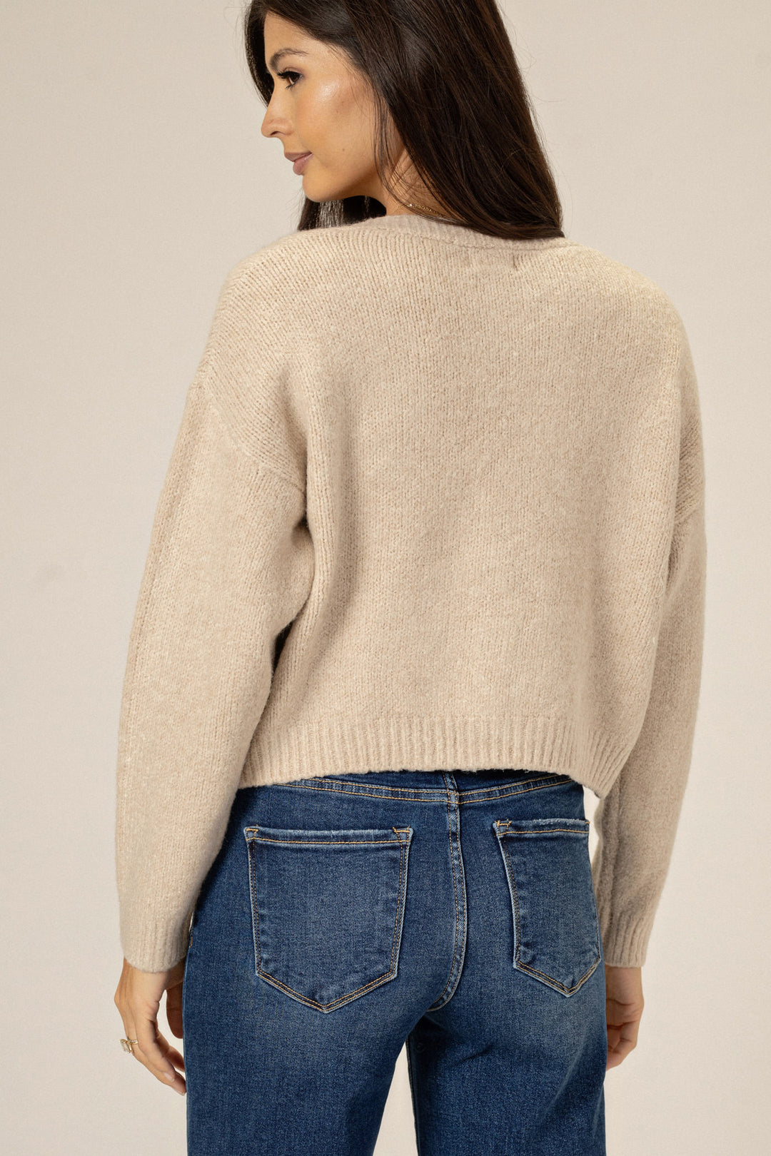 A warm, beige knit cardigan with a buttoned front, worn by a woman with long, dark hair in a side profile view.
