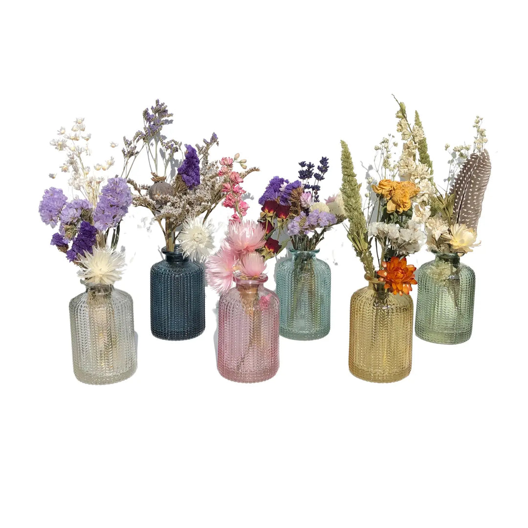 Assorted dried flower bouquets in varying colored glass bottles with unique textures and shapes.