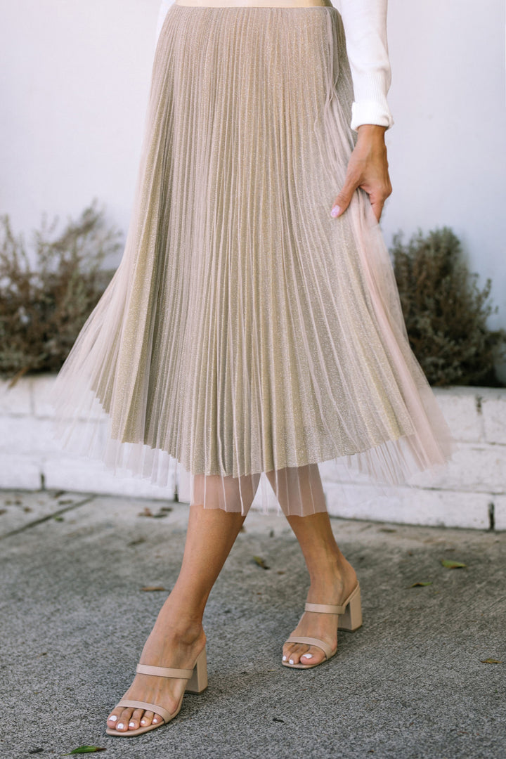 Shimmering gold pleated midi skirt with delicate texture and flowing silhouette, paired with strappy nude sandals.