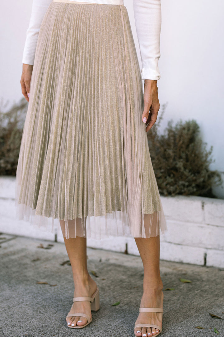 Gold pleated midi skirt with sheer overlay and ankle strap sandals.