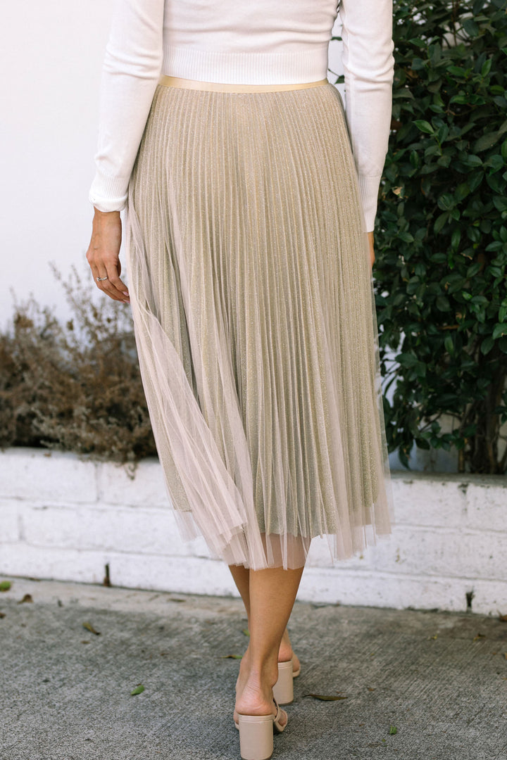 Pleated gold midi skirt with sheer overlay, worn with a white top and nude heels.