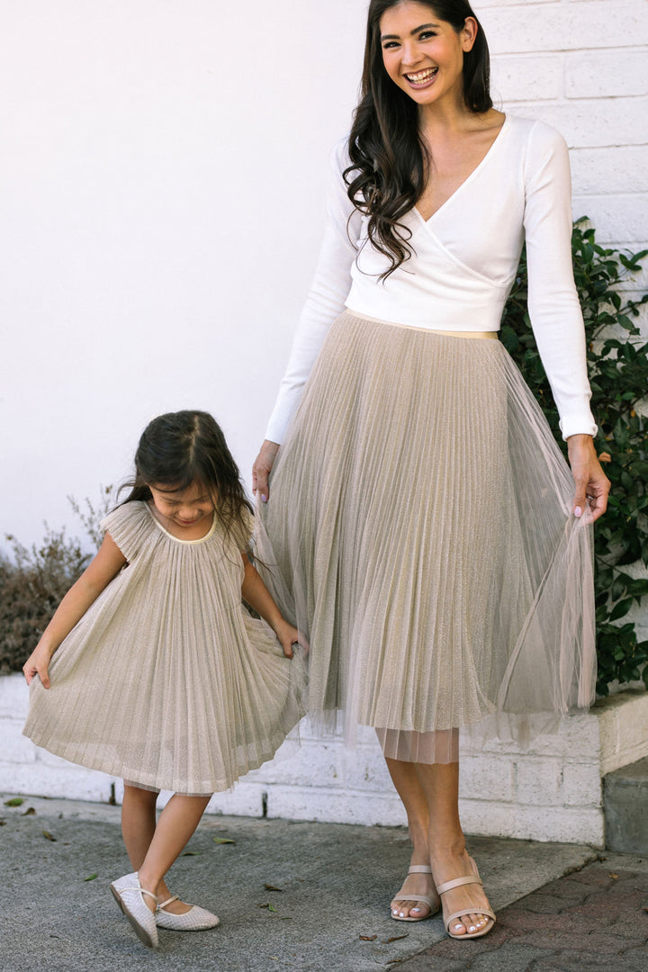 Two girls wearing matching pleated skirts in a light beige color, walking together and smiling.