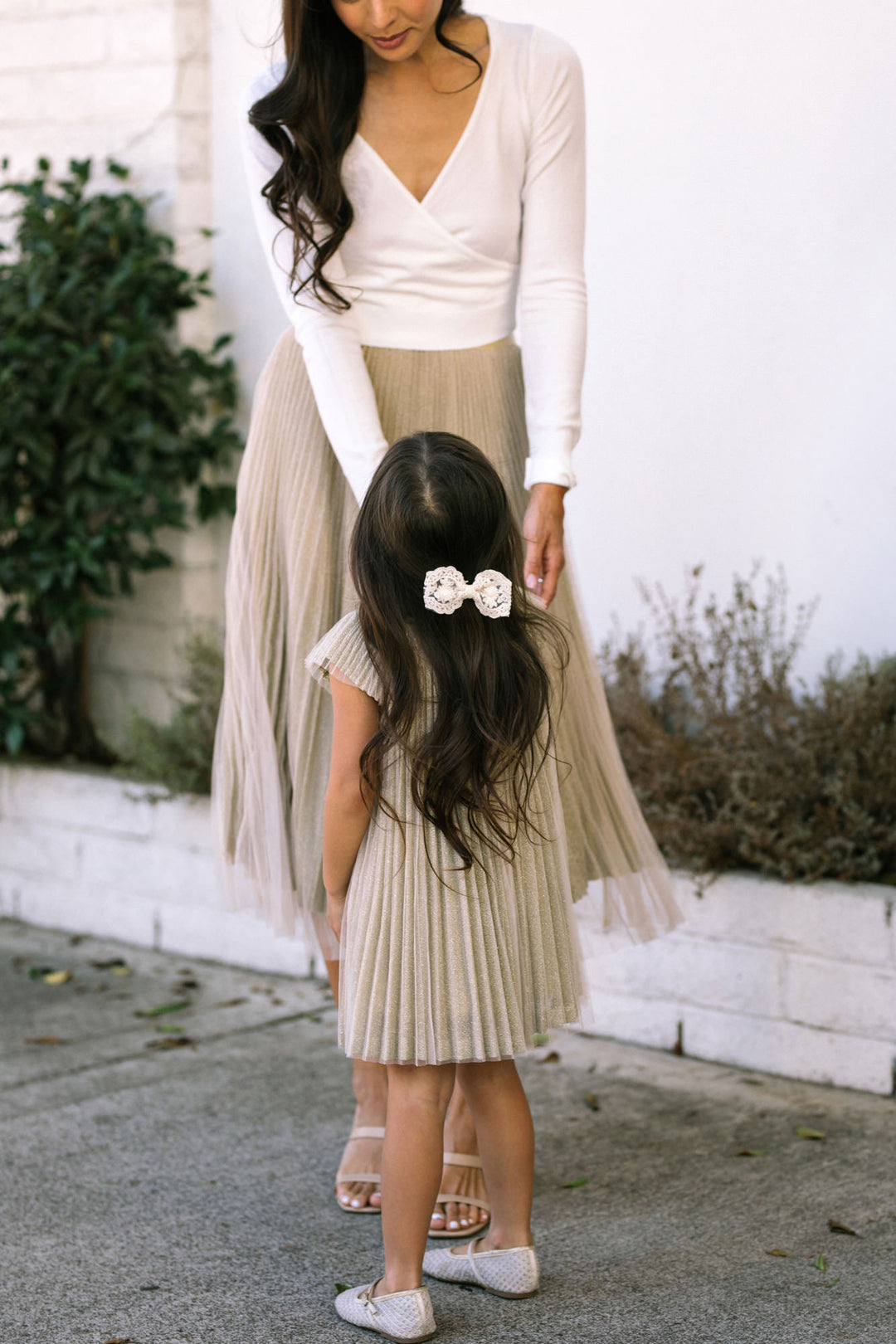 Young girl wearing a pleated, beige skirt and a white top, with a decorative hair accessory.