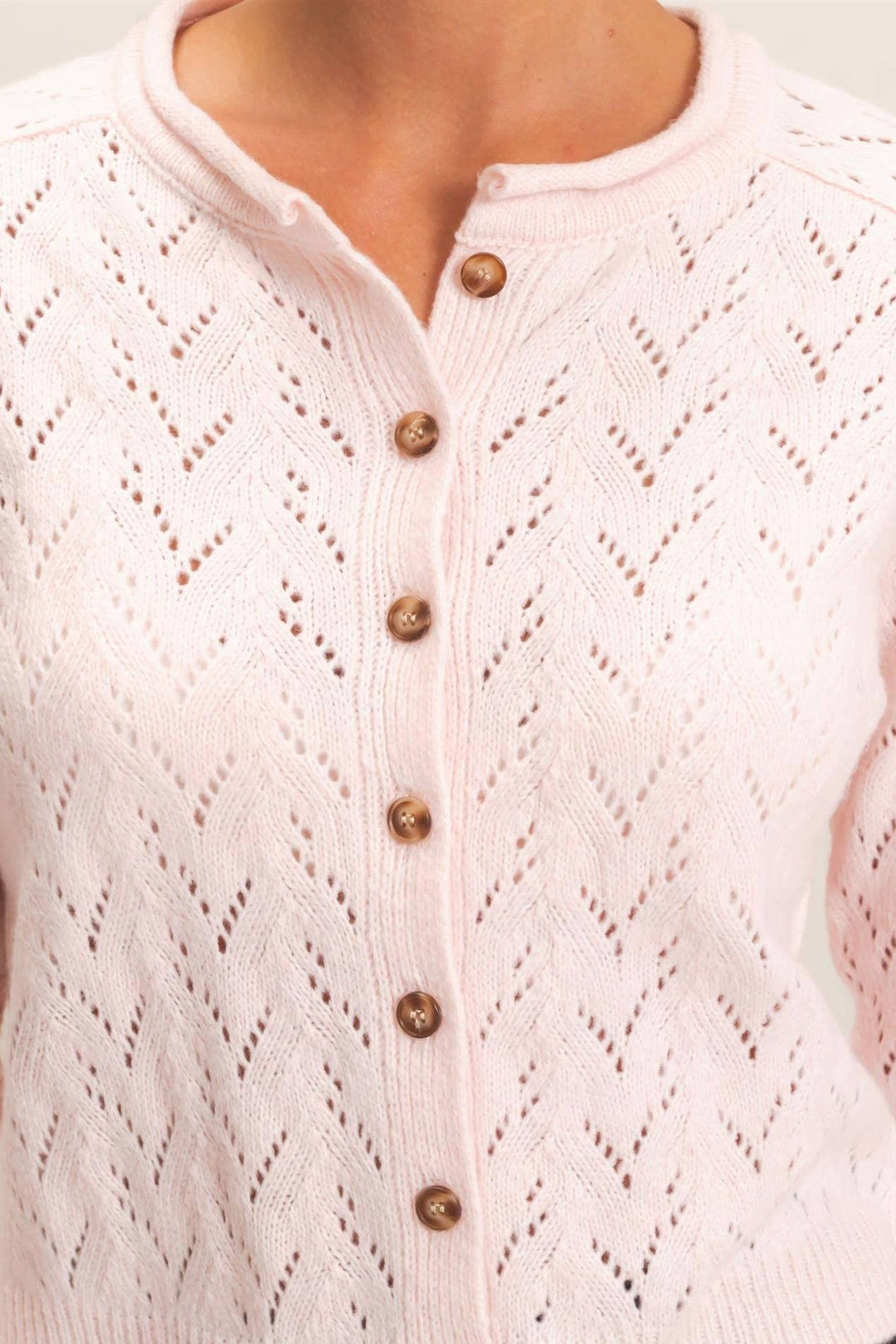 A light pink knit cardigan sweater with a textured openwork chevron pattern and brown buttons, shown on a model.