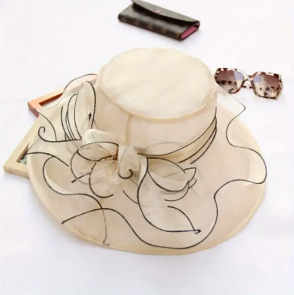 Cream-colored hat with floral print and curving black lines, adorned with a decorative accent piece.