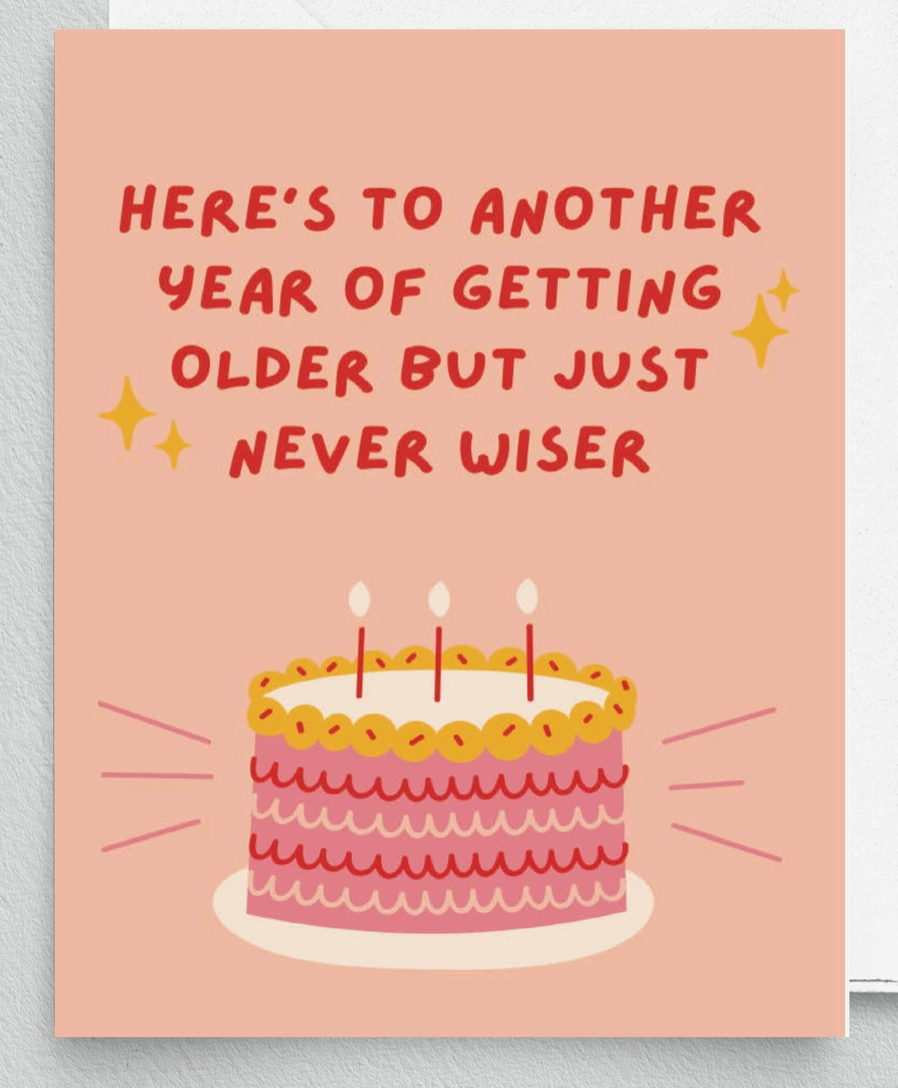 A pink greeting card with a birthday cake, text stating "Here's to another year of getting older but just never wiser", and sparkle accents.