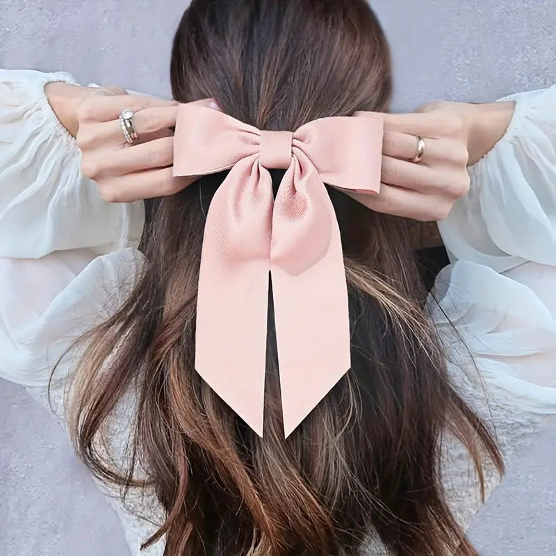 A close-up view of a woman's dark hair adorned with a large, soft pink bow hair clip, adding a stylish and feminine touch.