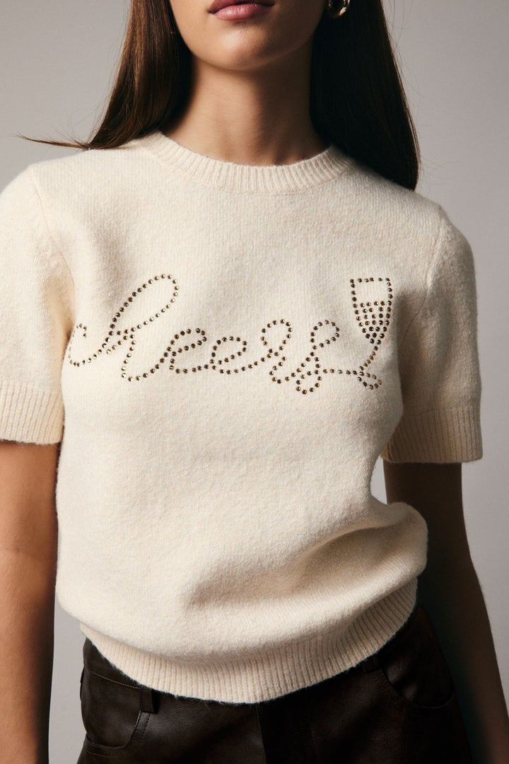 A soft, cream-colored knit sweater with a rhinestone "Cheers" graphic design across the front, featuring a classic crew neckline and short sleeves.