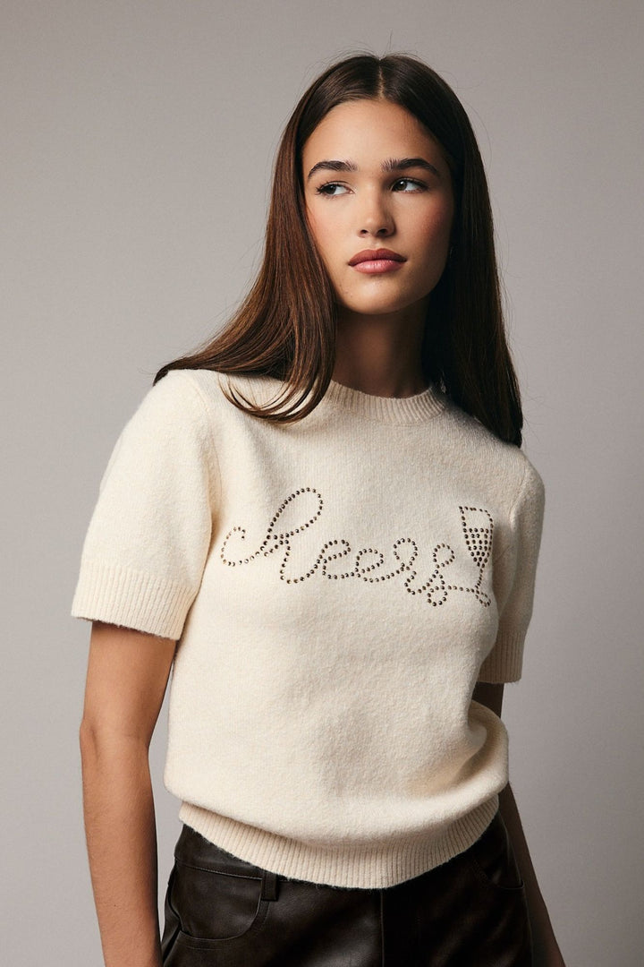 A close-up image of a model wearing a white knit top with rhinestone text that reads "Cheery" across the chest.