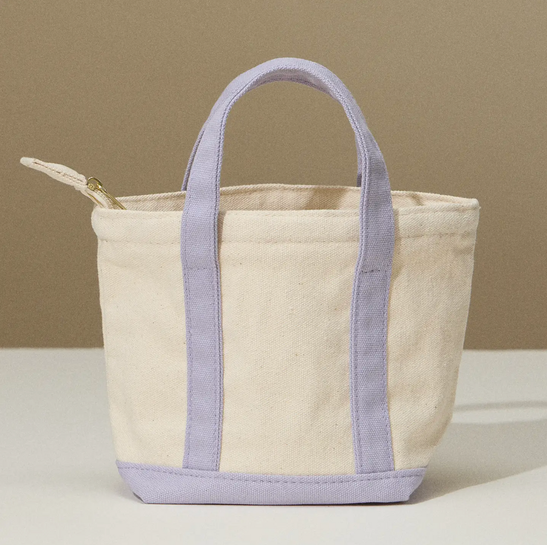 Cream-colored canvas tote bag with lavender handles and zippered compartment, designed for everyday use.