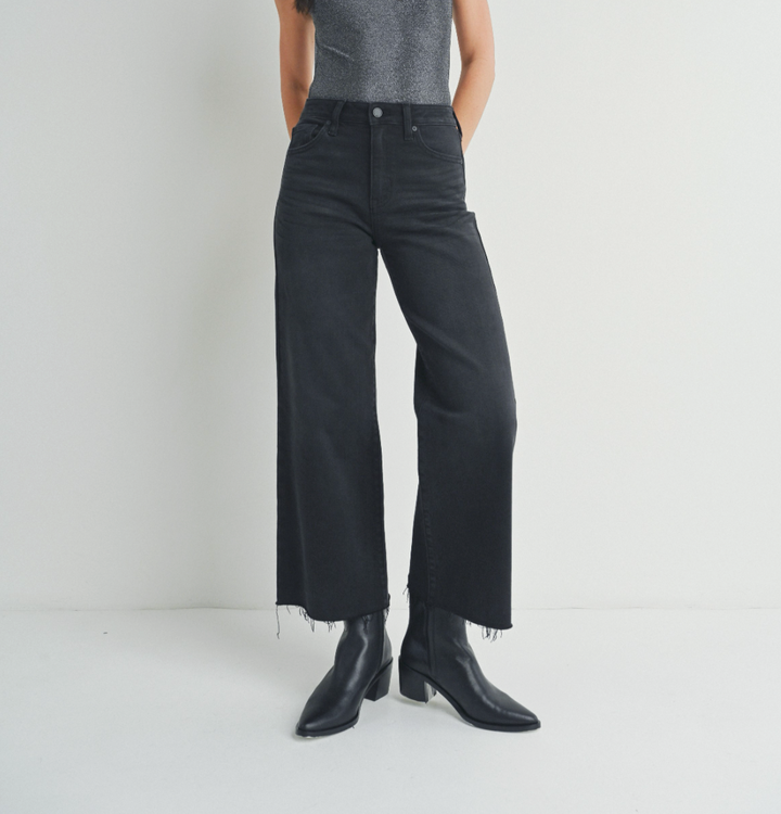 Model wearing dark wide-leg jeans with a sleeveless grey top and black leather boots.