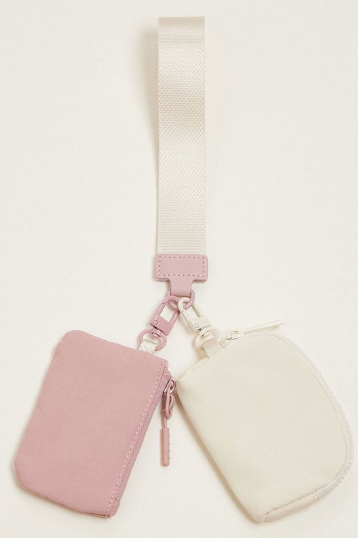 A compact dual-pouch wristlet in soft pink and cream colors, with a detachable strap for versatile carrying.