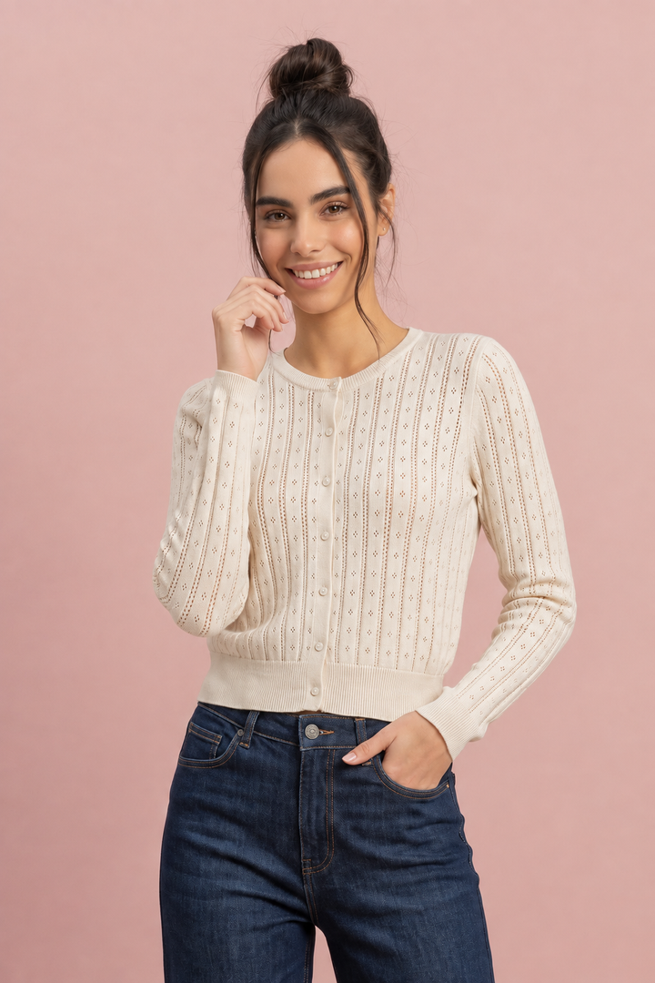 Cream pointelle knit cardigan with button front, worn with dark jeans, front view on pink background.