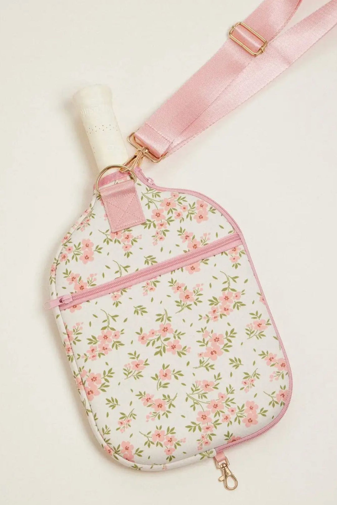 A soft pink and white neoprene pickleball paddle bag with a delicate floral print and gold-toned hardware.