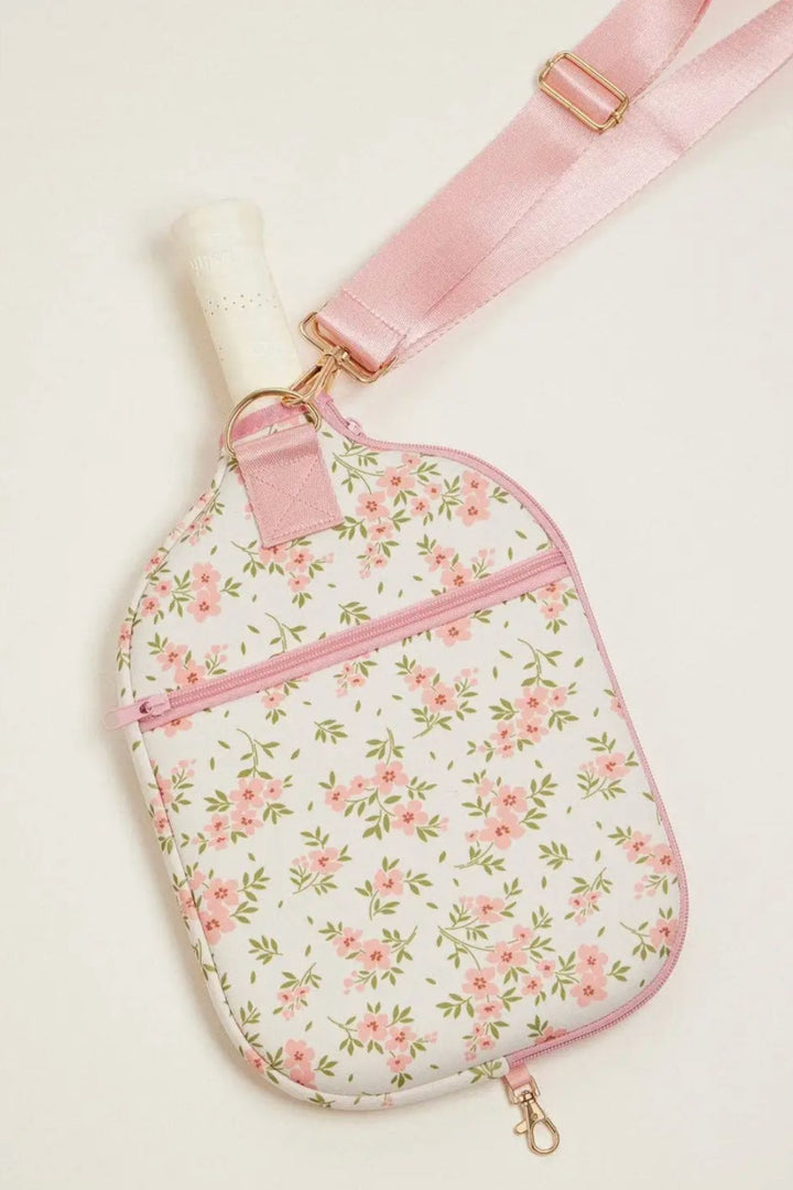 A soft pink and white neoprene pickleball paddle bag with a delicate floral print and gold-toned hardware.
