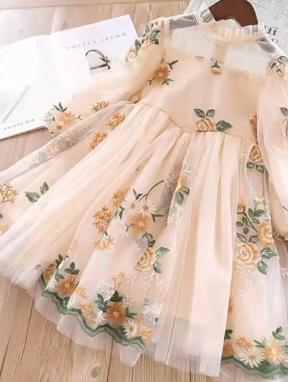 Delicate white dress with vibrant floral embroidery, featuring long sleeves and a flowing, full skirt.