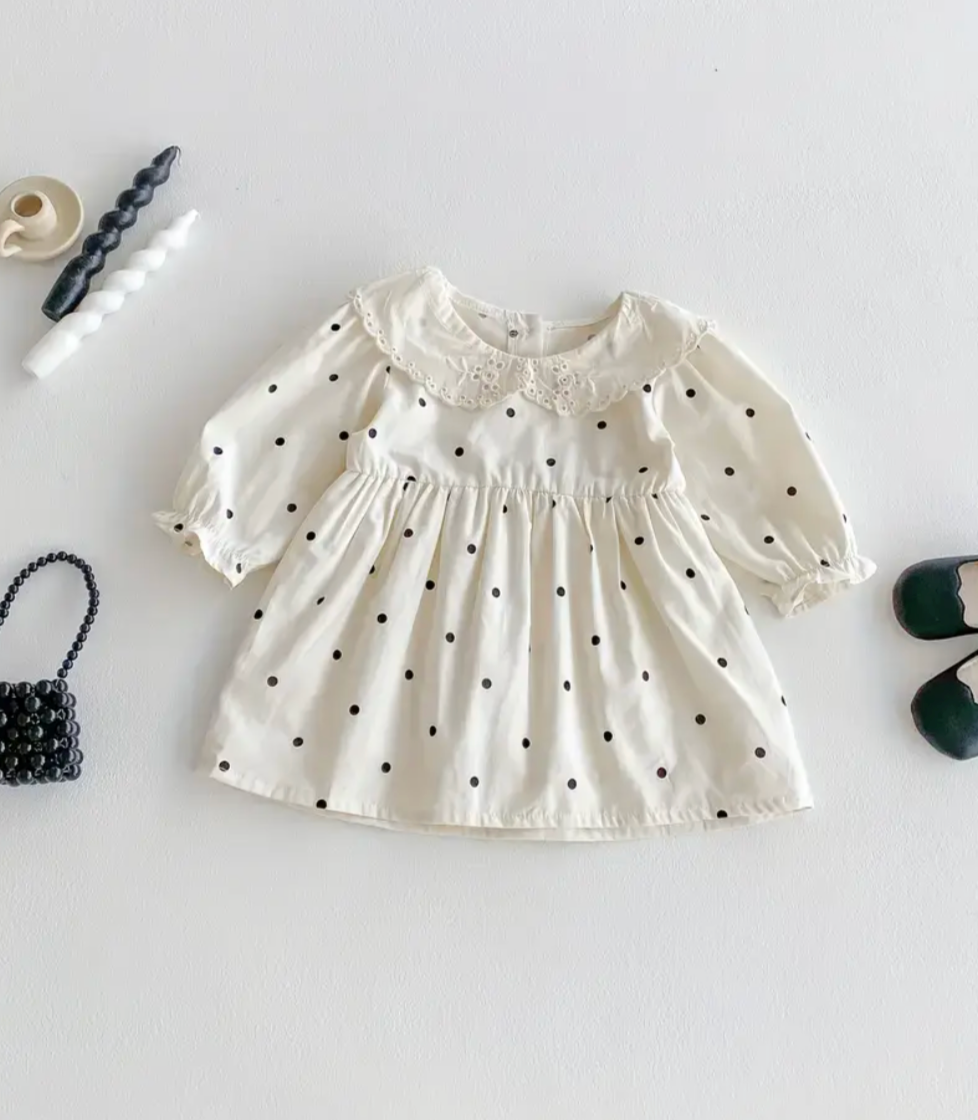 White girls' dress with black polka dots, puffy long sleeves, and eyelet lace detail at the neckline.