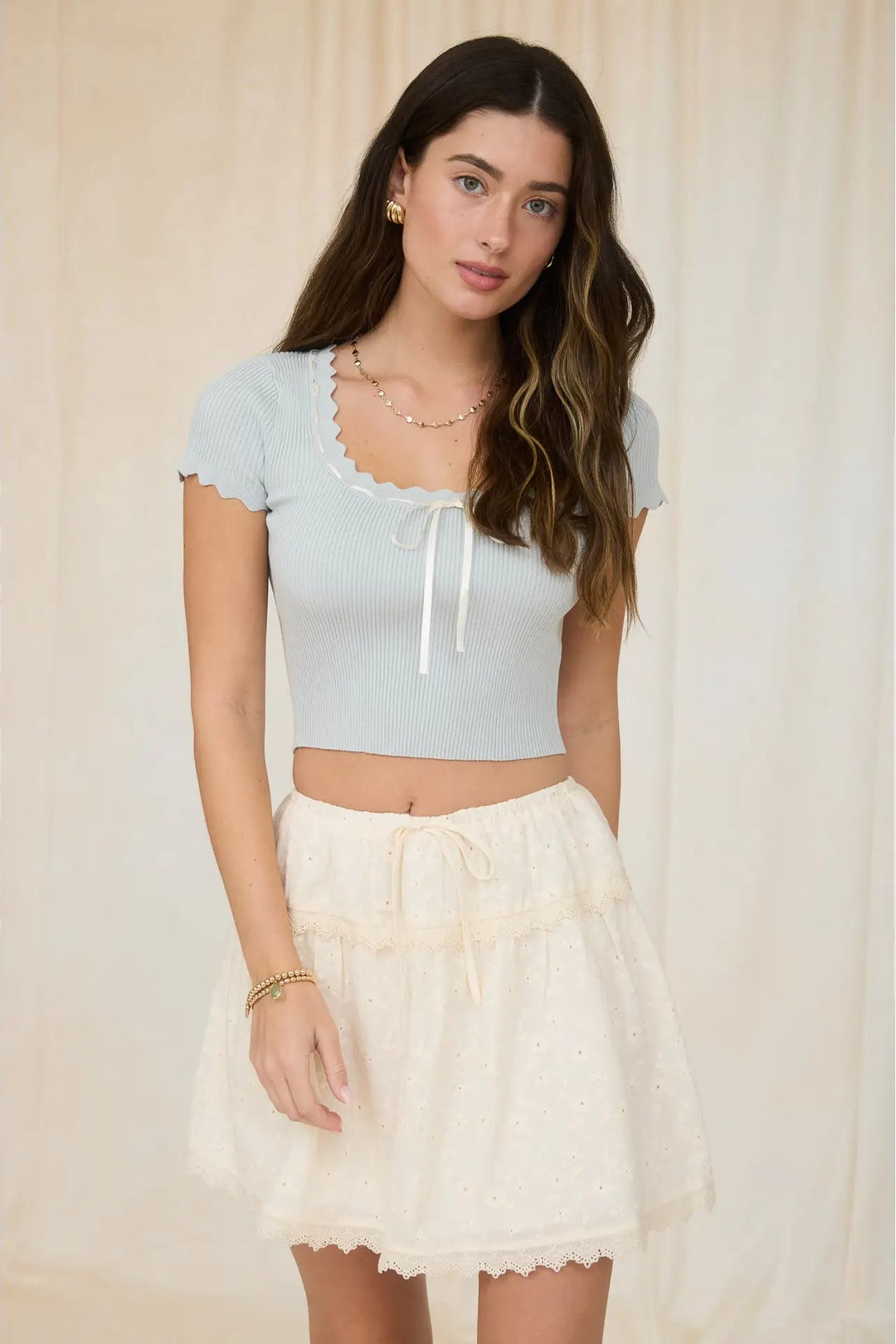 Woman wearing a light blue crop top and white lace skirt against a neutral background