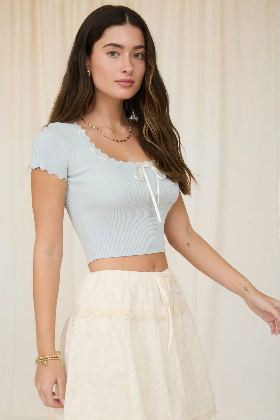 Woman wearing a light blue top and beige skirt against a neutral background