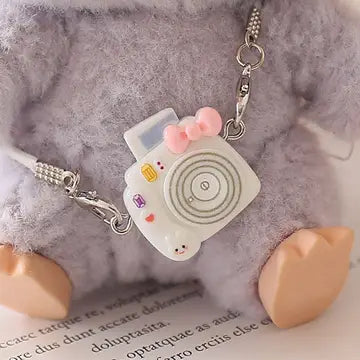 White toy camera charm with colorful buttons on fuzzy gray background.
