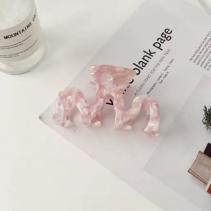Pink marble-patterned resin claw clip with a swirled design, measuring approximately 3.5 inches by 2 inches.