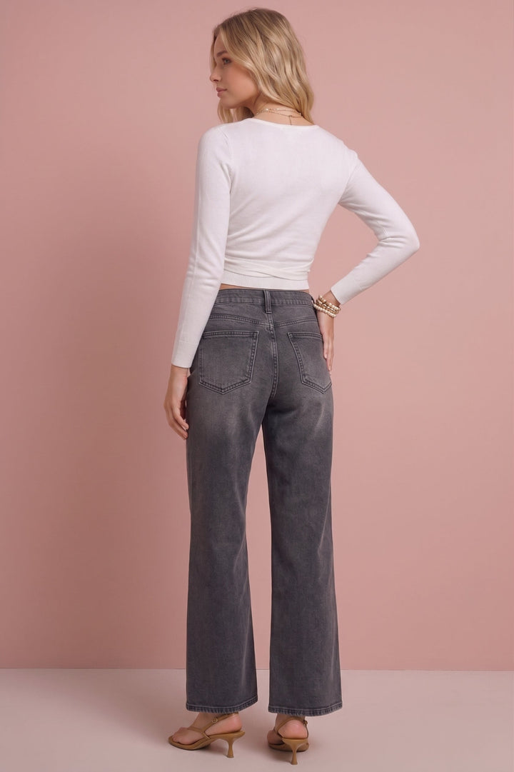 A woman shown from the back wearing a white long-sleeve crop top and dark gray wide-leg jeans, standing against a solid dusty pink studio background.