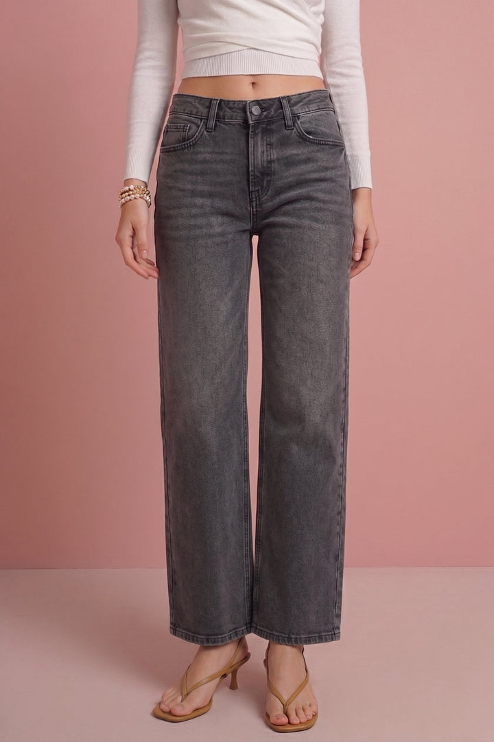 A model wearing dark gray wide-leg cropped jeans, a white long-sleeve crop top, and tan heeled sandals, standing against a solid pink studio background.