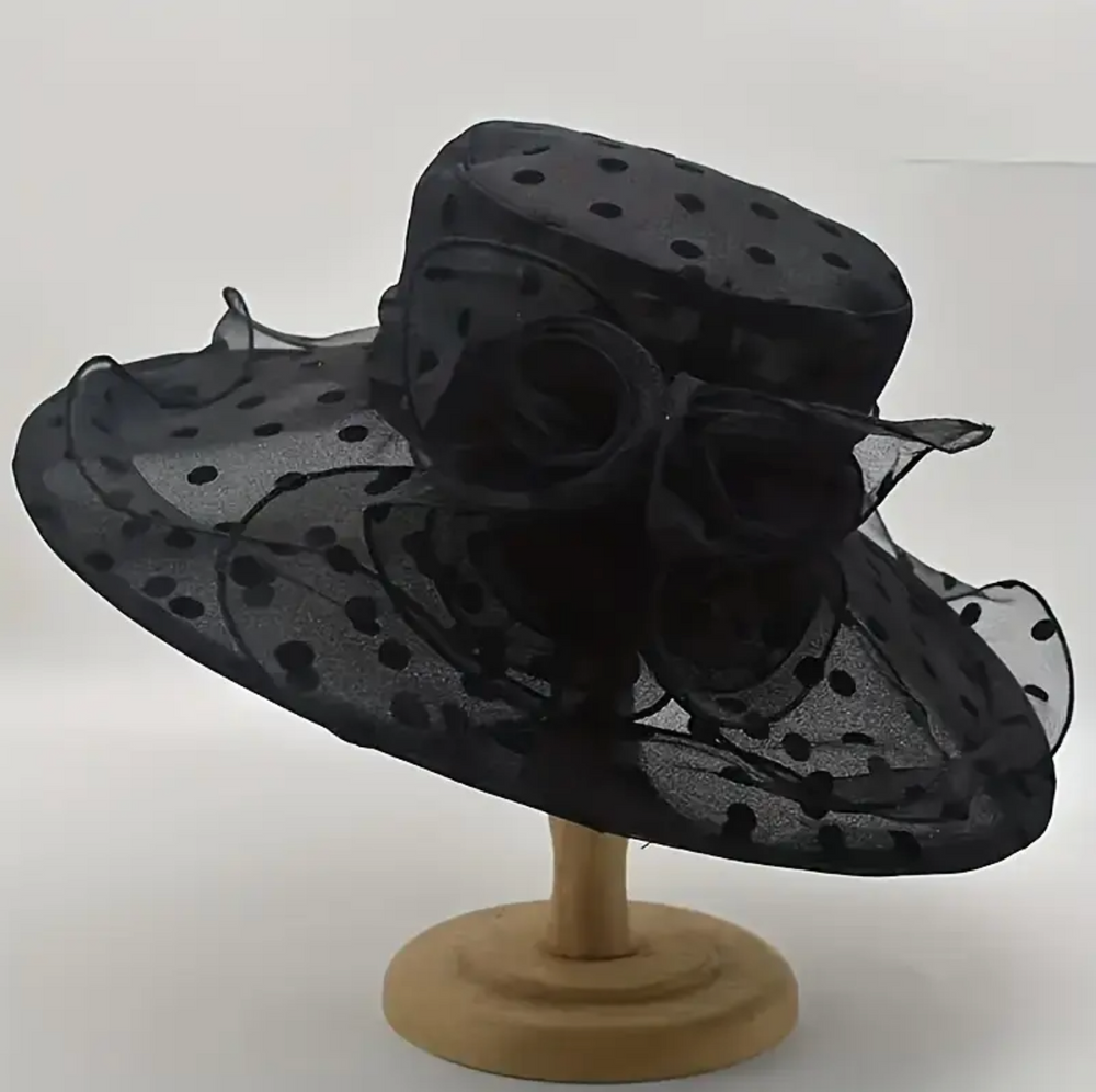 A black wide-brimmed derby hat with a polka dot pattern, featuring a ribbon trim and subtle floral detailing.