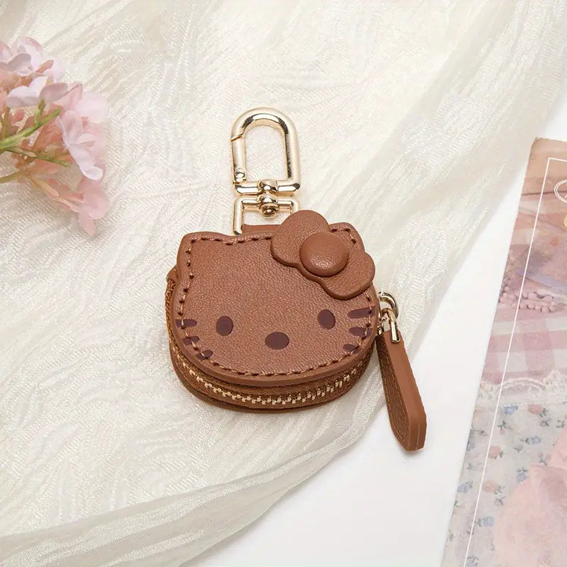 A brown leather keychain with a gold zipper pull and an embossed Hello Kitty character face design.