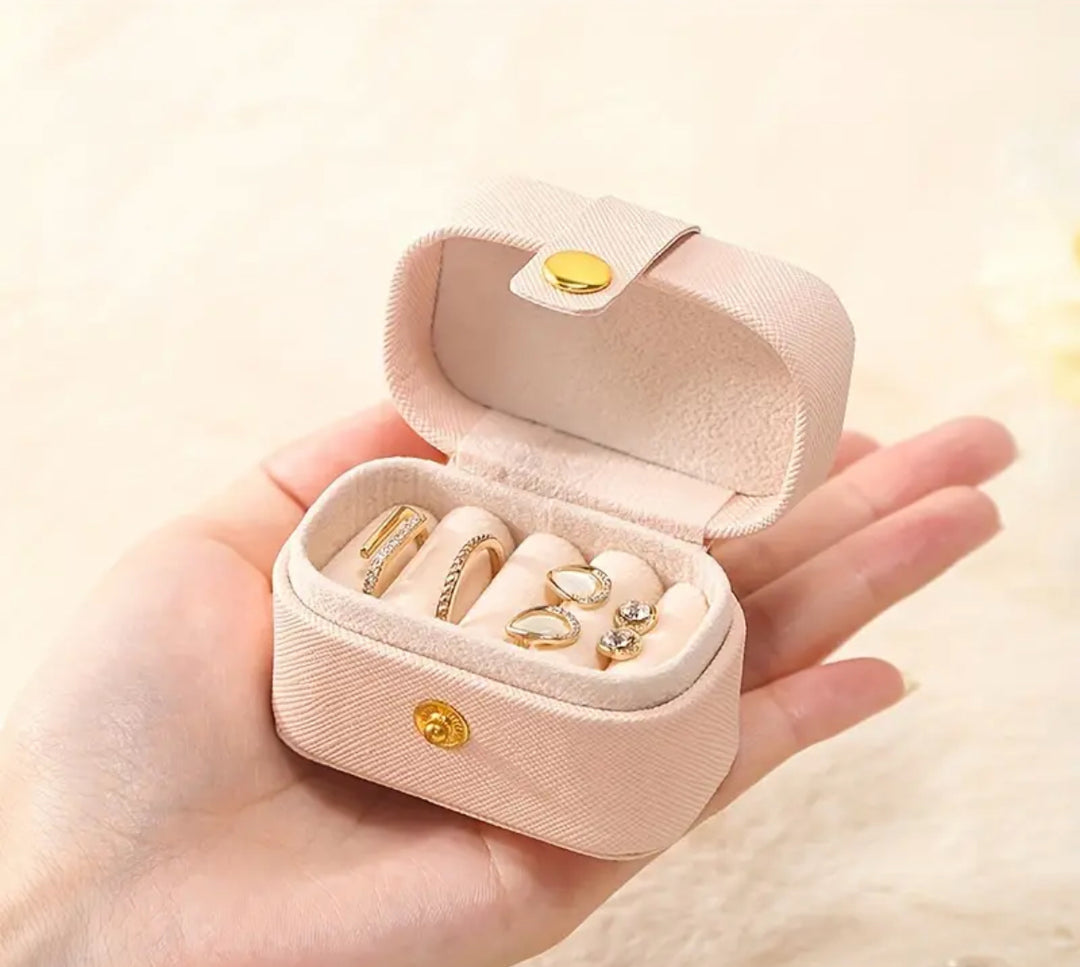 Compact pink jewelry box with golden latch, featuring cubbies for storing rings, necklaces, and other accessories.