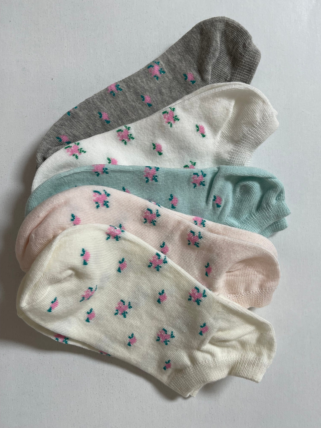 A stack of three pastel-colored ankle socks with a floral print pattern in shades of pink and mint green.