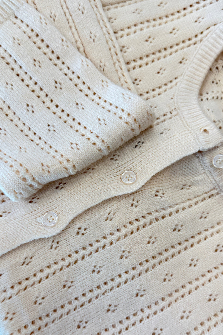 Cream pointelle knit cardigan with button details, folded flat lay view.