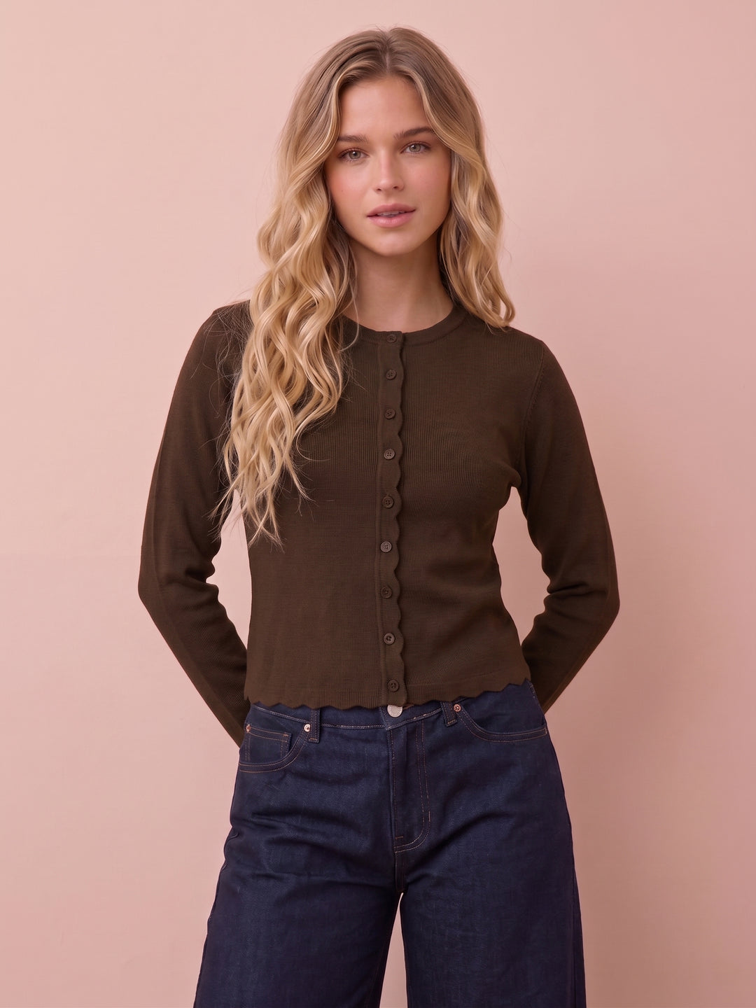 Brown ribbed cardigan with scalloped edges worn with dark jeans, front view.